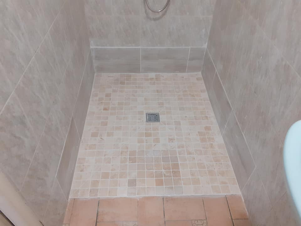 Douche à l'italienne carrelée en travertin avec receveur en mosaïque.