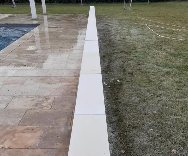 Margelles en pierre claire bordant une plage de piscine en travertin.