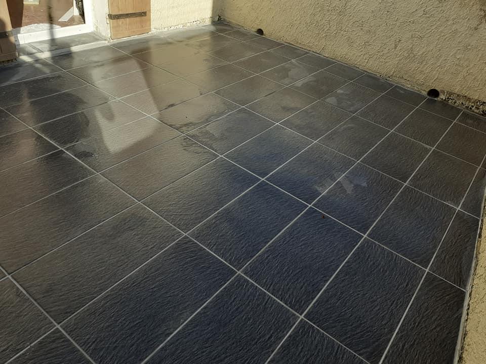 Terrasse extérieure carrelée en grès aspect ardoise, joints réguliers.